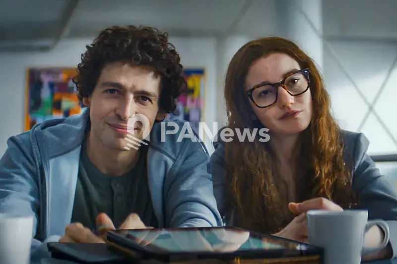 Sam Bankman-Fried (played by Anthony Boyle) and Caroline Ellison (played by Julia Garner) sitting together at a table.