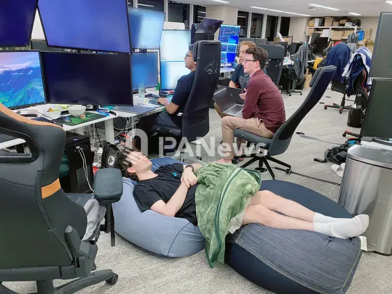 Sam Bankman-Fried sleeps on bean bag chairs in the FTX Hong Kong office while employees work at their desks in the background.
